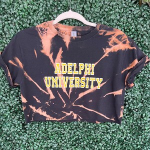 ADELPHI UNIVERSITY black bleach crop tee with white and yellow letters.