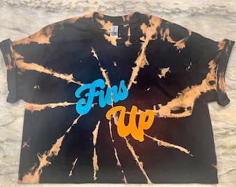 May include: A black tie-dye cropped t-shirt with the words "Fins Up" in blue and orange lettering.