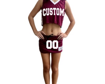 Könnte beinhalten: Ein maroonfarbenes Basketballtrikot mit weißen Verzierungen und dem Wort "CUSTOM" auf der Vorderseite. Das Trikot ist gekürzt und wird mit einem passenden maroonfarbenen Rock mit einer weißen Nummer "00" auf der Vorderseite kombiniert.