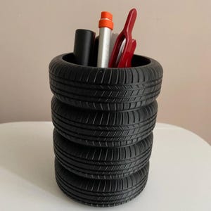 May include: Black tire-shaped desk organizer with four stacked tires. The organizer is filled with pens and pencils.