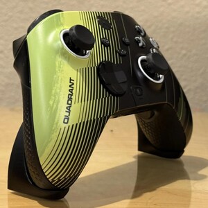 May include: A black and green Xbox controller with a custom design featuring black and yellow stripes and the word "QUADRANT".