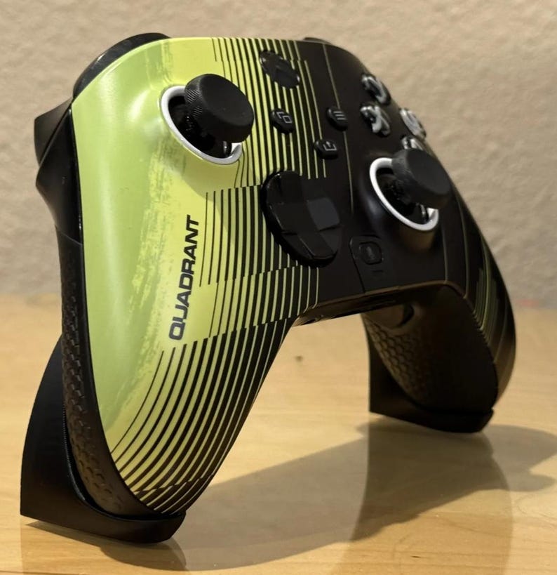 May include: A black and green Xbox controller with a custom design featuring black and yellow stripes and the word "QUADRANT".