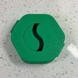May include: A green hexagonal container with a green S-shaped cutout in the center.