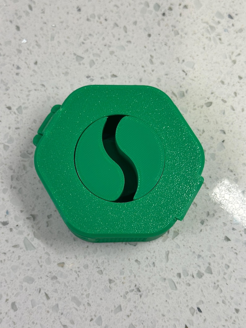 May include: A green hexagonal container with a green S-shaped cutout in the center.