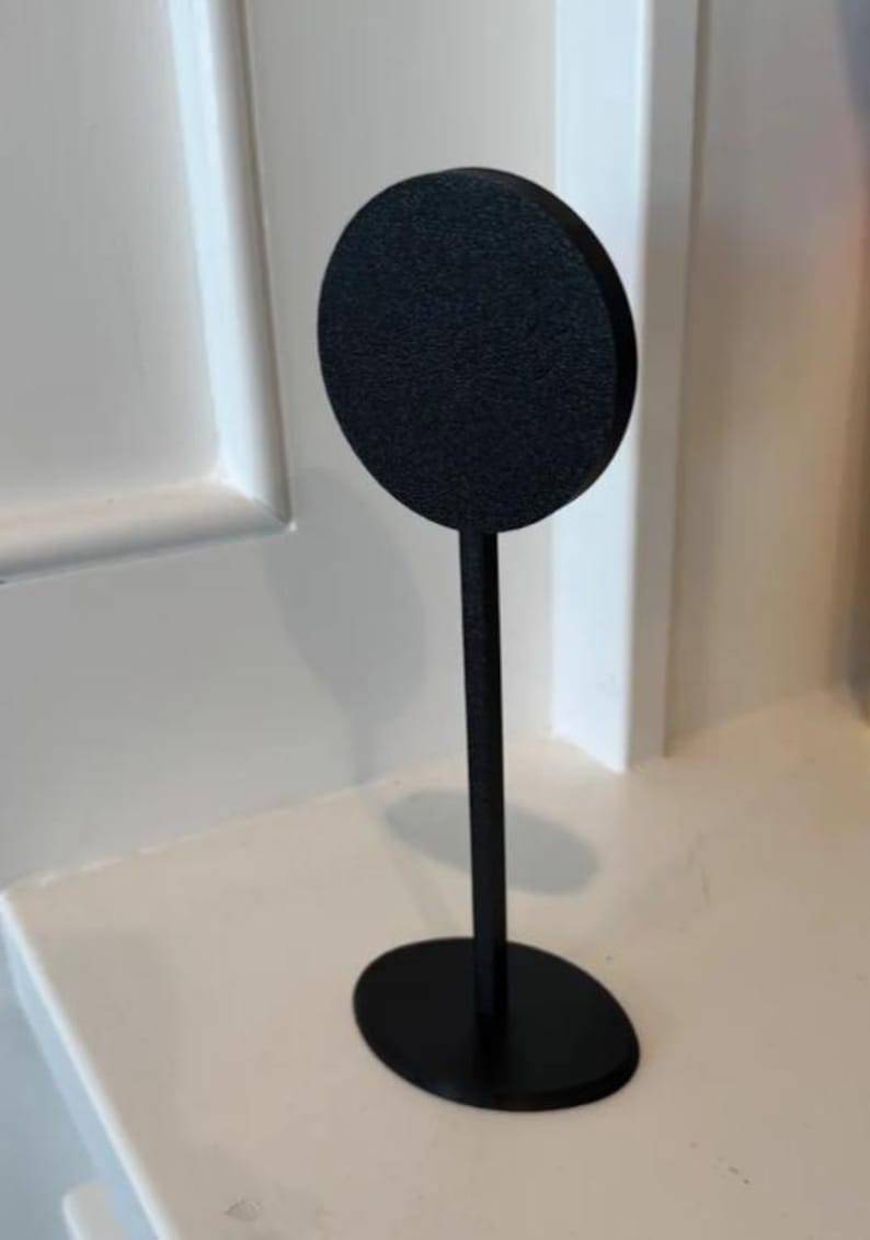 May include: A black metal display stand with a round top and an oval base.
