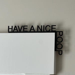 Puede incluir: Un letrero de madera negro con el texto "Have a nice poop" escrito en él. El letrero está montado en una puerta blanca.