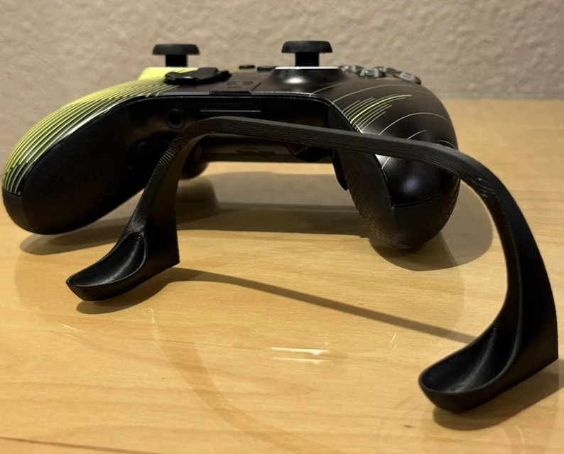May include: A black and yellow Xbox controller with a black plastic stand. The stand is designed to hold the controller upright.