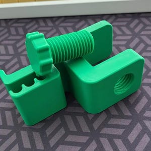 Puede incluir: Un juego de tornillos y soportes impresos en 3D de color verde brillante. El tornillo tiene una cabeza hexagonal y un v&aacute;stago roscado. Los soportes tienen un agujero y una ranura para que encaje el tornillo. El juego est&aacute; dise&ntilde;ado para aplicaciones mec&aacute;nicas o de construcci&oacute;n.