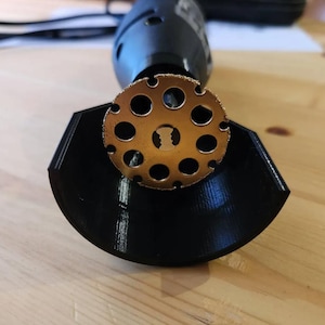 Puede incluir: Primer plano de una fresa rotativa de color dorado con una carcasa de plástico negro. La fresa tiene una forma circular con varios agujeros alrededor del borde.