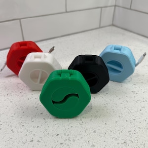 May include: Five cable organizers in different colors: red, white, black, light blue, and green. Each organizer is shaped like a hexagon and has a slot for a cable to be fed through.