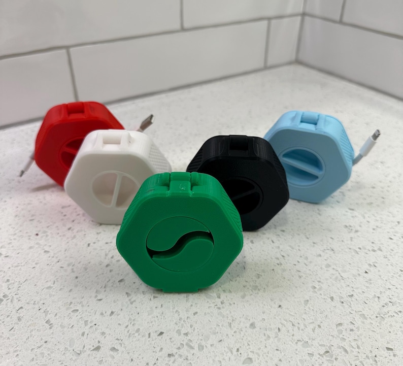 May include: Five cable organizers in different colors: red, white, black, light blue, and green. Each organizer is shaped like a hexagon and has a slot for a cable to be fed through.