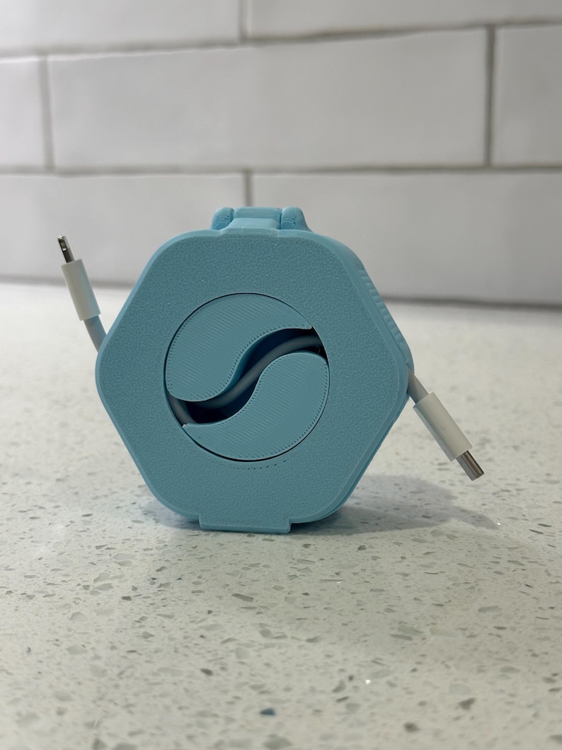 May include: A light blue cable organizer with a hexagonal shape and a circular opening in the center. The cable is white and is partially wound around the organizer.