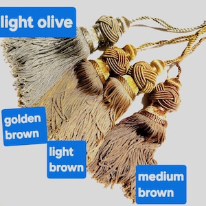 May include: Four decorative tassels with knotted heads and hanging cords, labelled light olive, golden brown, light brown, and medium brown. Each tassel features a dense cluster of fine, silky threads hanging from a structured, woven knot top.