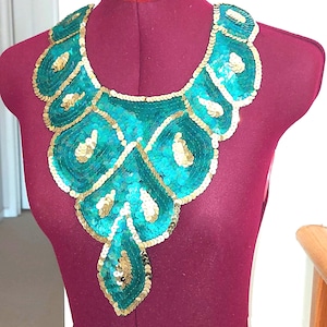 May include: A teal and gold sequined embellishment for clothing. The embellishment is shaped like a teardrop and has a scalloped edge.