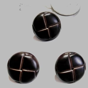Peut inclure: Trois boutons sphériques brun foncé avec un motif cousu en forme de grille. Les boutons sont disposés sur une surface gris clair. Une pièce de monnaie argentée est visible en arrière-plan.