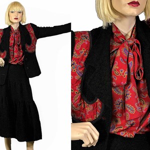 May include: A black blazer with a paisley patterned trim and a matching black skirt. The blazer has a shawl collar and a single button closure. The skirt is a-line and has a tiered design.