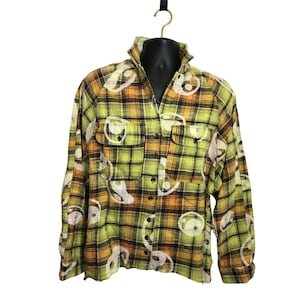 May include: A long-sleeve button-up shirt featuring a plaid pattern in shades of lime green, orange, and black. The fabric is decorated with a repeating white circular graphic print. The shirt includes a collar and two chest pockets with flaps.