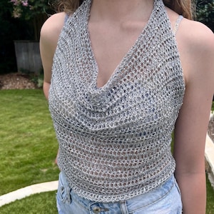 May include: A silver halter top with a cowl neck. The top is made of a chainmail-like material, creating a mesh effect. The top is sleeveless and has a low neckline. The top is paired with blue denim shorts.