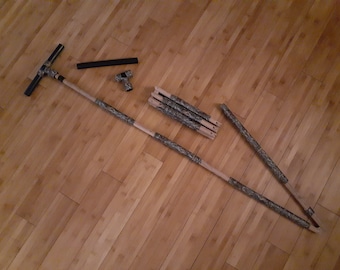 May include: A set of wooden poles with camouflage tape, a black pipe, and a black T-shaped connector. The poles are used to build a tripod.