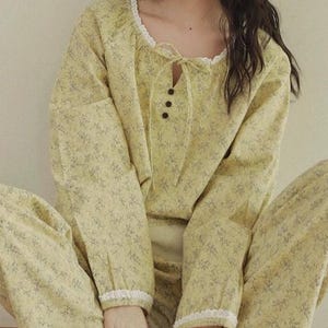 May include: Yellow floral pyjama set featuring a long-sleeved top and matching trousers. The top has a lace-trimmed neckline and button detail. The pyjamas are made of a soft, lightweight fabric, ideal for relaxing.