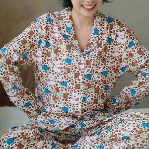 May include: A beige pajama set with a repeating pattern of cartoon bears and leopard spots. The long-sleeved top has a button-down front and a collar. The matching pants complete the set. The pajamas are made of a soft material.