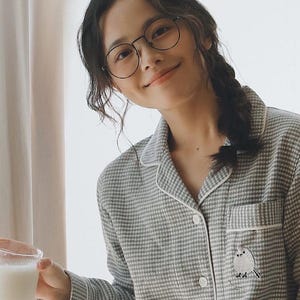May include: A person wearing round glasses and a grey and white checked pajama set. The pajama top has a small bird embroidery on the pocket. The person is holding a glass of milk.