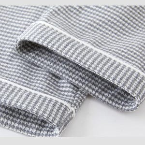 May include: Close-up of grey and white houndstooth fabric with white trim. The fabric is folded over, showing the hem and cuff of a garment. The pattern is a classic, small-scale check.
