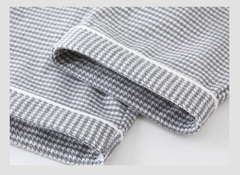 May include: Close-up of grey and white houndstooth fabric with white trim. The fabric is folded over, showing the hem and cuff of a garment. The pattern is a classic, small-scale check.