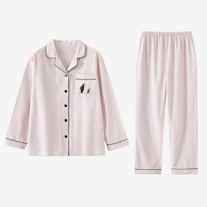 May include: A light pink pajama set with a penguin design. The long-sleeved top has black trim and buttons, with a pocket featuring an embroidered penguin. The matching pants have a comfortable elastic waistband and black trim.