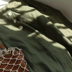 Pu&ograve; includere: Gonna verde oliva con tre bottoni grandi e una borsa tote in pelle marrone con un design a rete. La gonna &egrave; realizzata in un tessuto morbido e fluido. La borsa ha un manico in corda colorata.