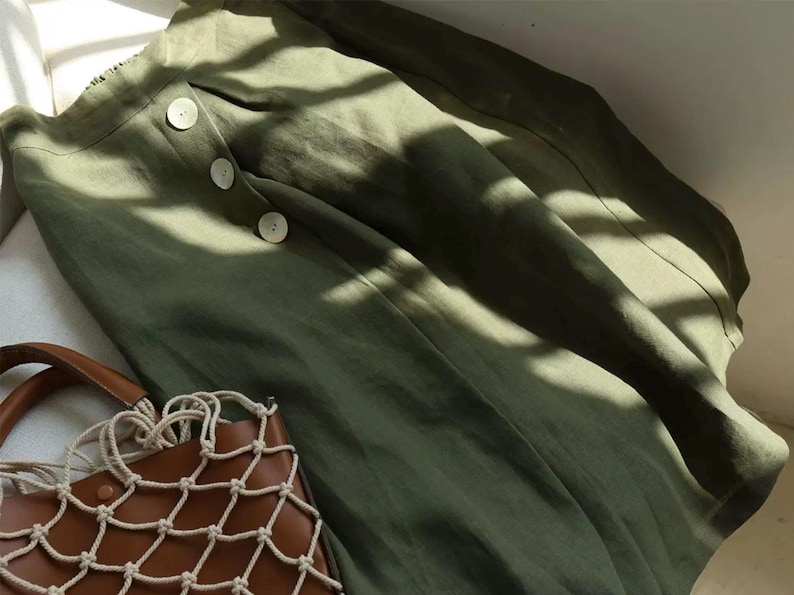 Pu&ograve; includere: Gonna verde oliva con tre bottoni grandi e una borsa tote in pelle marrone con un design a rete. La gonna &egrave; realizzata in un tessuto morbido e fluido. La borsa ha un manico in corda colorata.