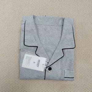 May include: Folded gray pajama set with black trim and a small pocket. The set includes a button-down shirt and pants. A white tag with the text "ETCOZY" is attached to the shirt.