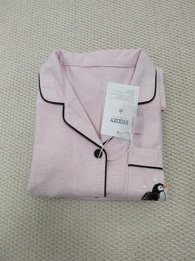 May include: Pink and white striped pajama set with black trim and a penguin embroidery. The set includes a collared shirt with a button closure and a pocket. The tag reads ETCOZY.