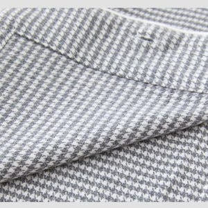 May include: Close-up of a grey and white houndstooth fabric. The fabric is folded, revealing the texture and pattern. The classic design features small, repeating checks, creating a textured appearance. The fabric appears to be a medium weight material.