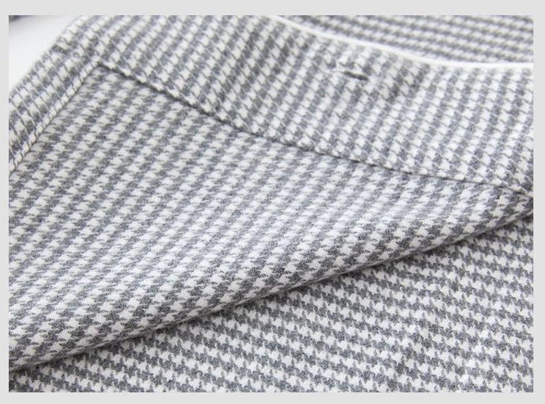 May include: Close-up of a grey and white houndstooth fabric. The fabric is folded, revealing the texture and pattern. The classic design features small, repeating checks, creating a textured appearance. The fabric appears to be a medium weight material.