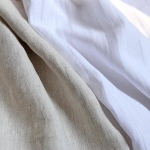 May include: Close-up of folded linen fabric in shades of beige and white. The fabric has a soft, textured appearance with visible weave details. The folds create shadows and highlights, adding depth to the image. Ideal for textile and home decor products.