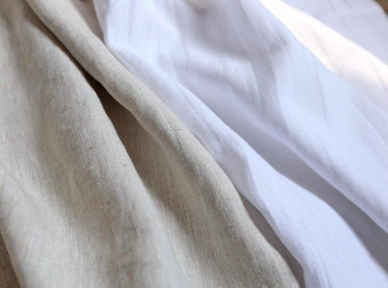 May include: Close-up of folded linen fabric in shades of beige and white. The fabric has a soft, textured appearance with visible weave details. The folds create shadows and highlights, adding depth to the image. Ideal for textile and home decor products.