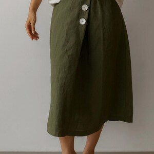 Pu&ograve; includere: Gonna a portafoglio verde oliva con tre grandi bottoni bianchi. La gonna &egrave; lunga fino al ginocchio ed &egrave; realizzata in un tessuto fluido. La modella indossa sandali bianchi con un piccolo tacco.