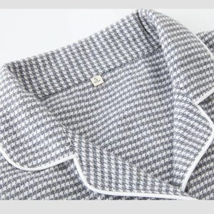 May include: Close-up of a grey and white houndstooth patterned pajama top with white trim. The collar and lapel are visible, along with a small tag labelled "S". The fabric has a soft, textured appearance.