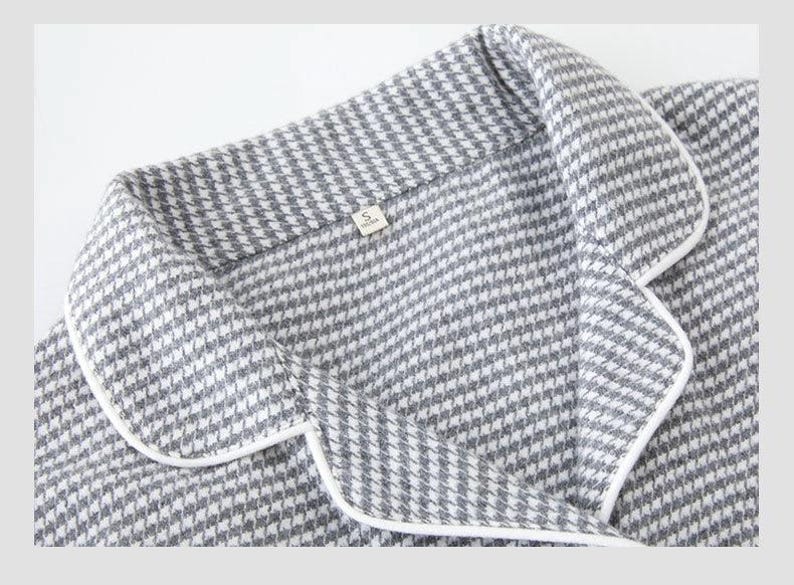 May include: Close-up of a grey and white houndstooth patterned pajama top with white trim. The collar and lapel are visible, along with a small tag labelled "S". The fabric has a soft, textured appearance.