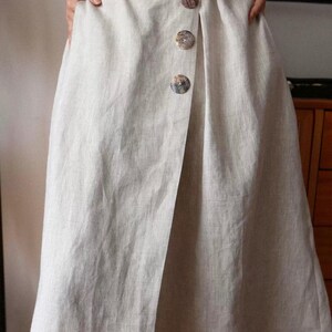 Pu&ograve; includere: Gonna in lino beige chiaro con design a portafoglio. La gonna presenta tre grandi bottoni decorativi sul davanti. Il tessuto sembra essere un lino naturale e strutturato. La gonna &egrave; lunga fino al ginocchio.