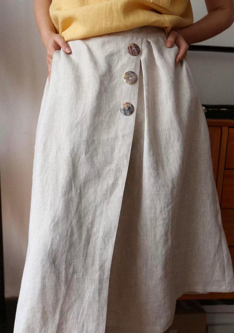 Pu&ograve; includere: Gonna in lino beige chiaro con design a portafoglio. La gonna presenta tre grandi bottoni decorativi sul davanti. Il tessuto sembra essere un lino naturale e strutturato. La gonna &egrave; lunga fino al ginocchio.