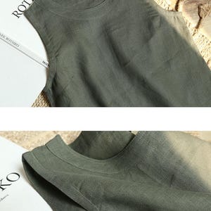 May include: A sleeveless, olive green linen top with a round neckline. The fabric has a slightly textured appearance. The top is displayed on a neutral background, with the word "ROTHKO" visible on a book in the background.