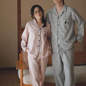 May include: Matching pajama sets in pink and gray. The pink set has a light stripe pattern, black trim, and a penguin graphic. The gray set has a similar design. Both sets include a button-down top and pants.