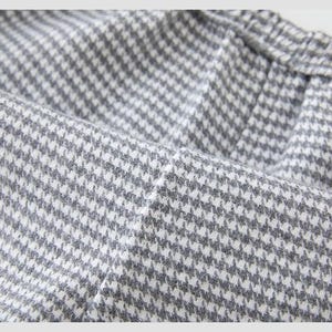 May include: Close-up of a grey and white houndstooth fabric. The fabric is folded, showing the texture and pattern of the material. The pattern is a classic, small-scale design.