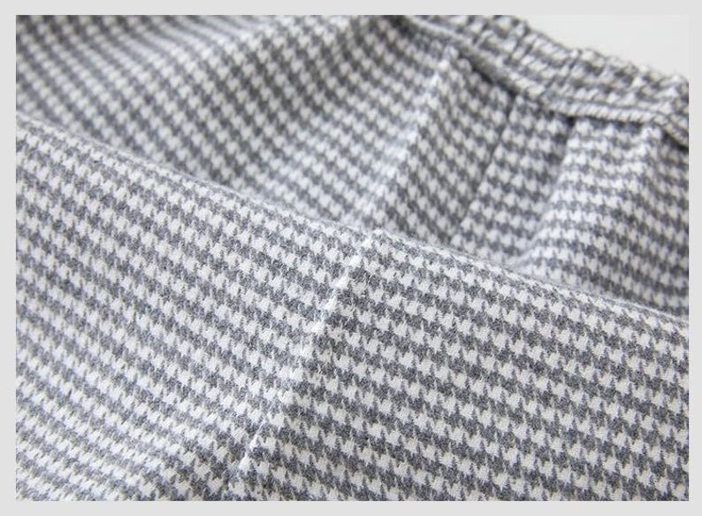 May include: Close-up of a grey and white houndstooth fabric. The fabric is folded, showing the texture and pattern of the material. The pattern is a classic, small-scale design.