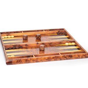 Pu&ograve; includere: Un tabellone da backgammon in legno con finitura in legno marrone. Il tabellone &egrave; aperto e mostra la superficie di gioco con strisce nere e gialle. Ci sono tre dadi sul tabellone, due marroni e uno bianco.