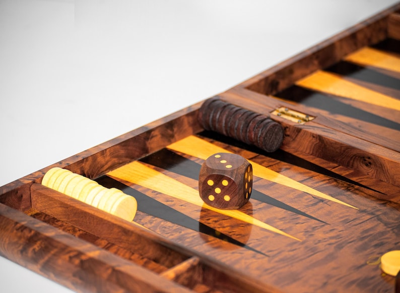 Pu&ograve; includere: Un tabellone da gioco di backgammon in legno con una superficie di gioco nera e gialla. Un solo dado con punti gialli &egrave; sul tabellone. Ci sono anche pile di pedine nei scomparti laterali.