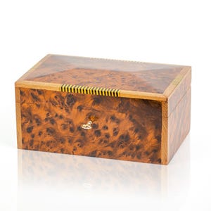 May include: A wooden box with a burl wood finish and a brass latch. The box has a decorative inlay of black and gold stripes around the top edge.