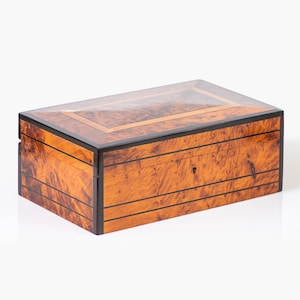 May include: A wooden box with a clear glass lid. The box is made of a light brown wood with dark brown accents. The box is rectangular in shape and has a smooth finish.